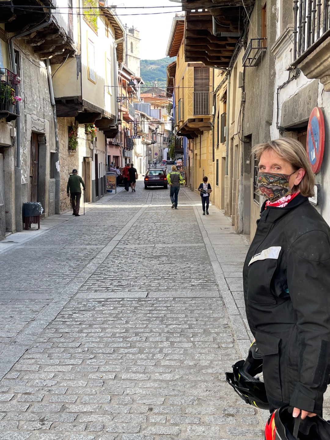 Woman in motorcycle gear with helmet on steep medieval cobblestone street, Candelario Spain